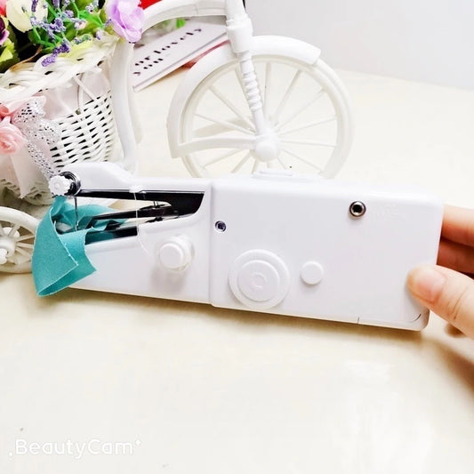 Máquina de costura portátil branca operada com uma mão, tecido azul e decoração com flores e bicicleta branca ao fundo